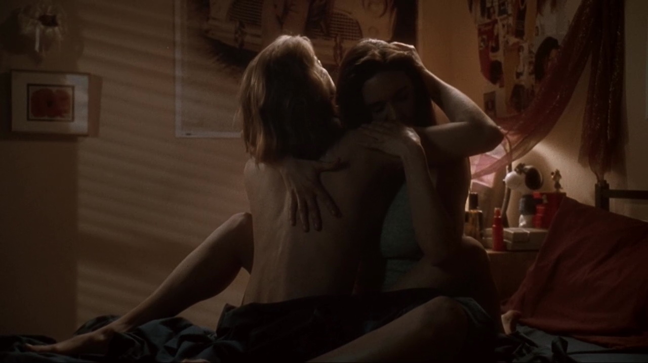 Kristy Swanson and Jennifer Connelly lesbian kissing while sitting on a bed together in a dorm room